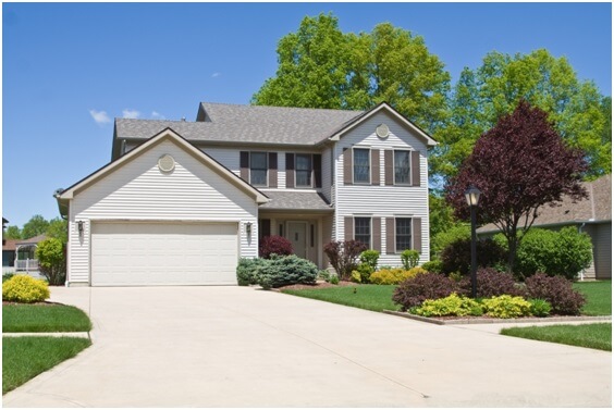 A white house surrounded by a beautiful lawn with a variety of bushes and trees.