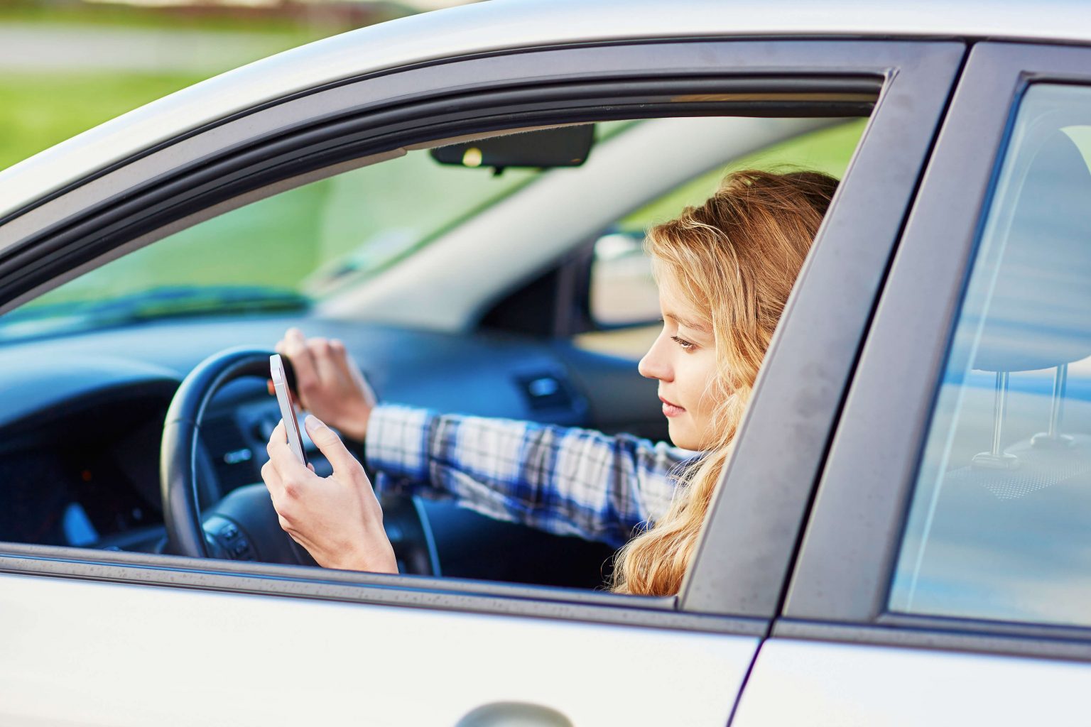 A woman driving while also looking at her phone.