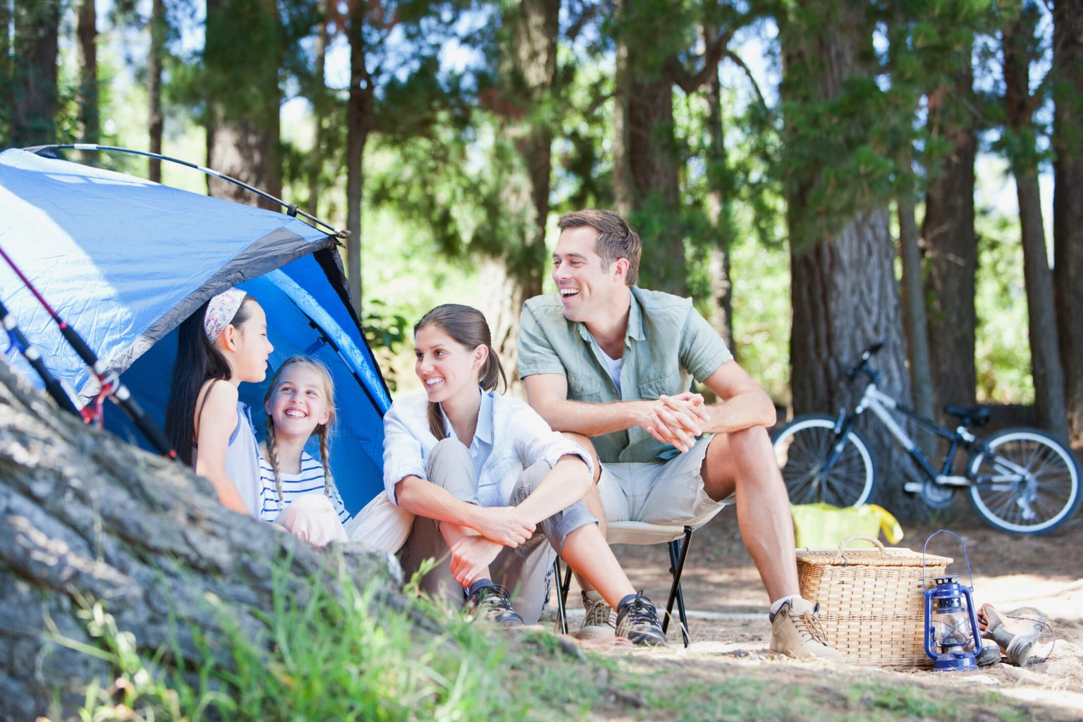 A family camping, sitting in front of a blue tent.