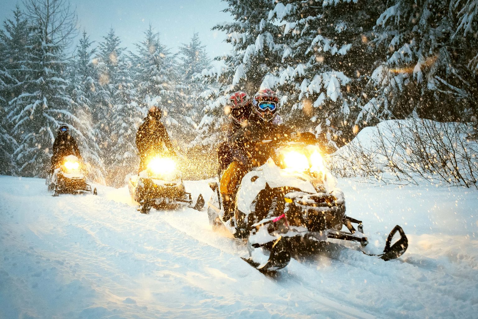 Three snowmobiles driving on a trail.