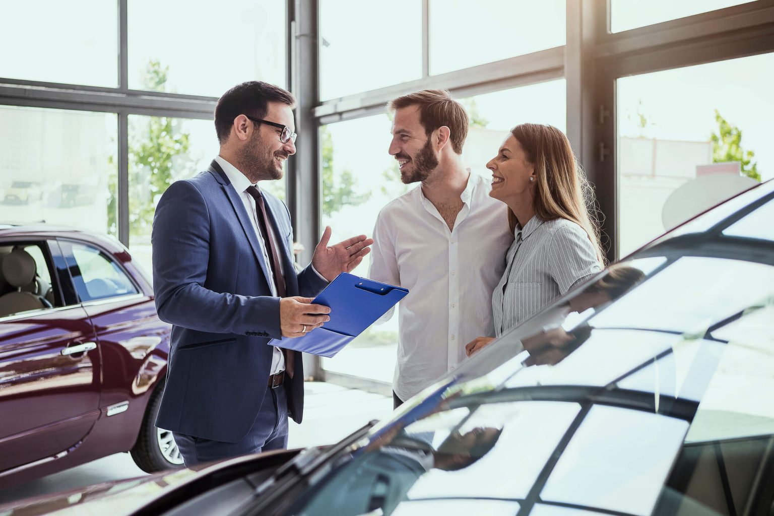 Business man talking to a couple at a car dealership