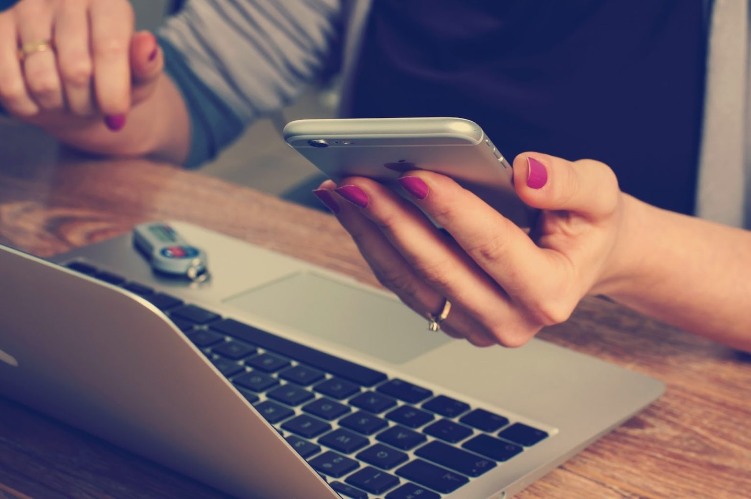 A woman holding her cell phone in front of a laptop.