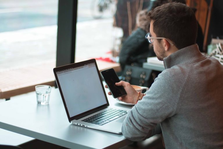 A man working on his laptop and holding his cell phone.