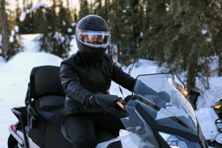 A person dressed in black with a black helmet riding a snowmobile.