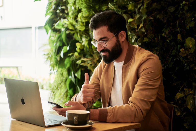 A man looking at a computer while giving thumbs up.