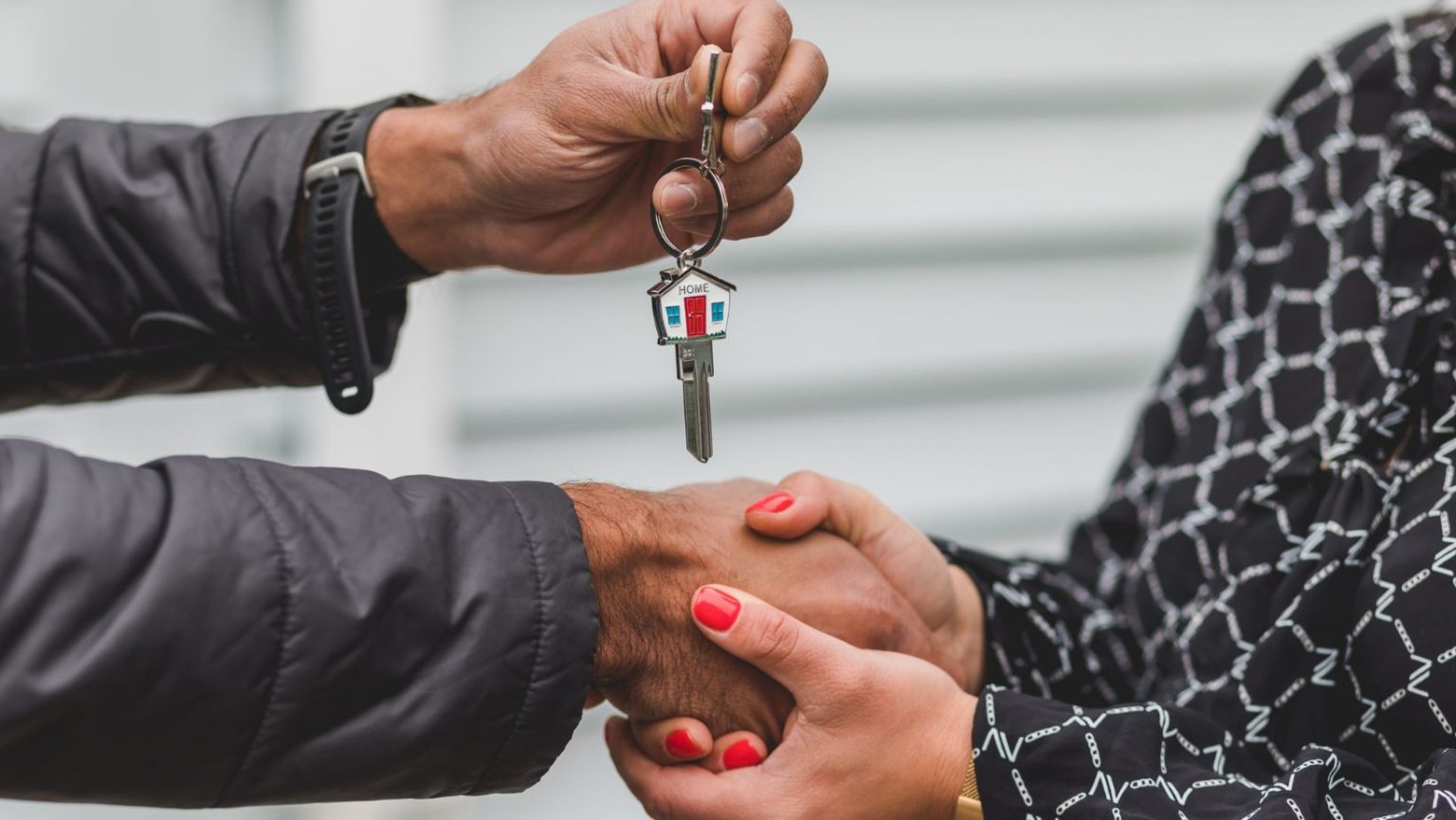 Two people shaking hands as the man hands a woman a house key.