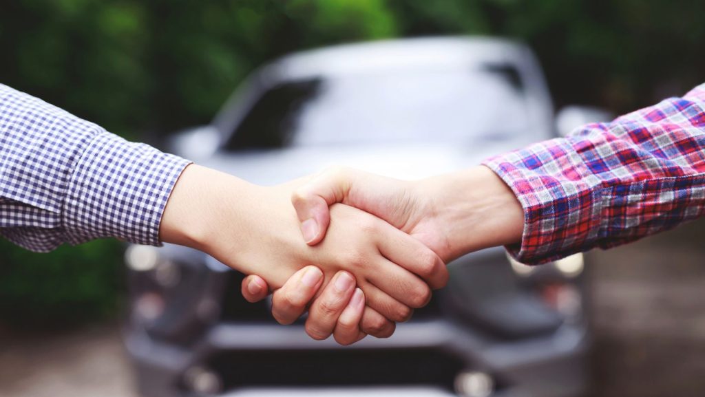 Two people shaking hands in front of a vehicle.