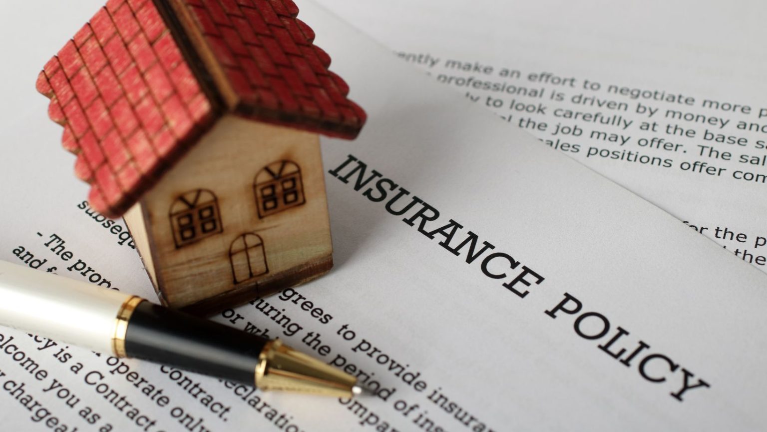 a small house model and pen sitting on top of insurance form policy