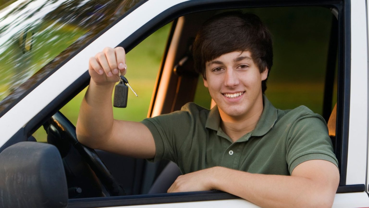 a teenager holding his car keys while sitting in the front seat of a car.