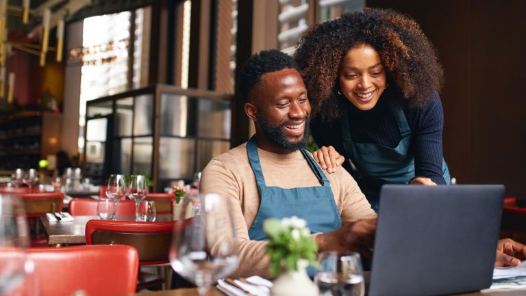 Two business owners looking at a laptop sitting in their restaurant