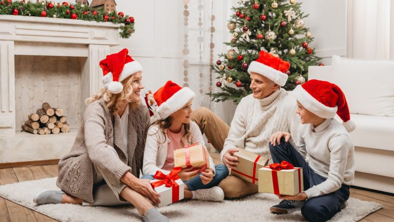 A family sitting on the floor with presents under a Christmas tree.