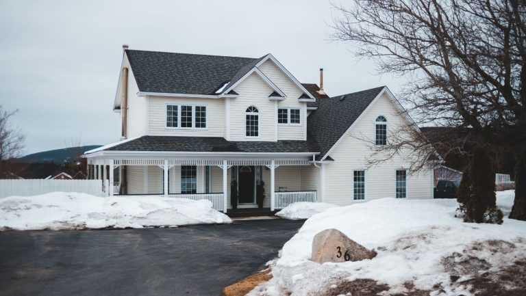 A white home in winter with snow surrounding it.