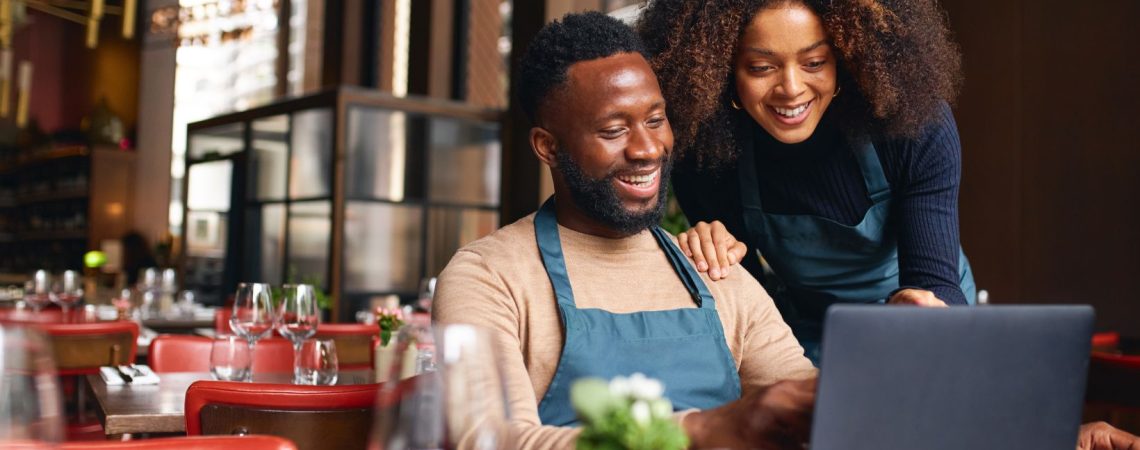 Two business owners looking at a laptop sitting in their restaurant