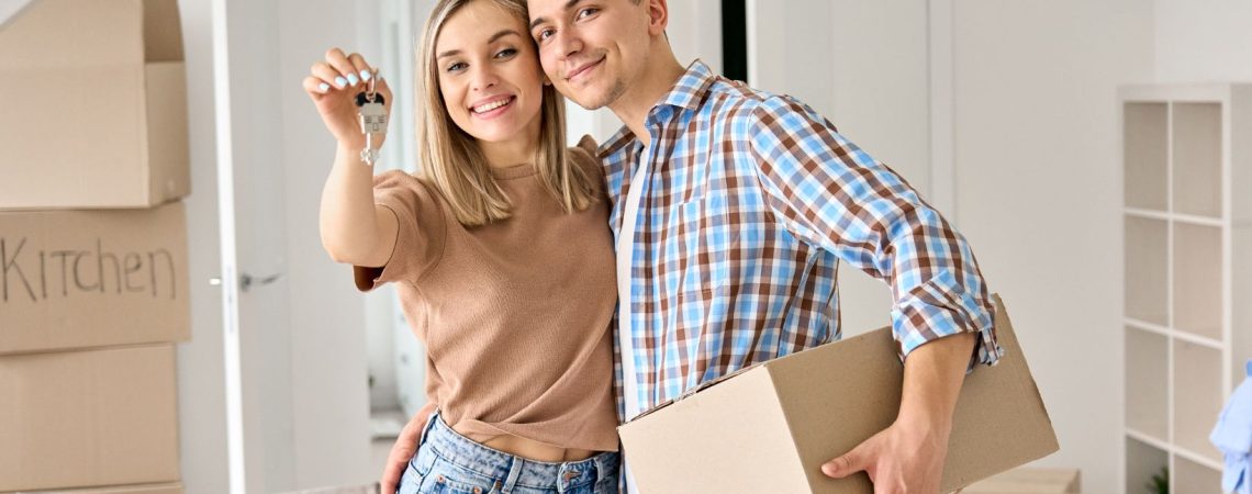 a couple holding up their new home keys, surrounded by moving boxes.