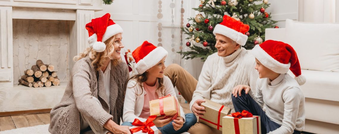 A family sitting on the floor with presents under a Christmas tree.