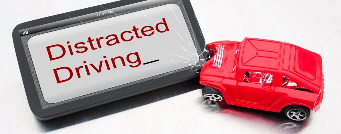 A toy car crashed into a tablet that says distracted driving.