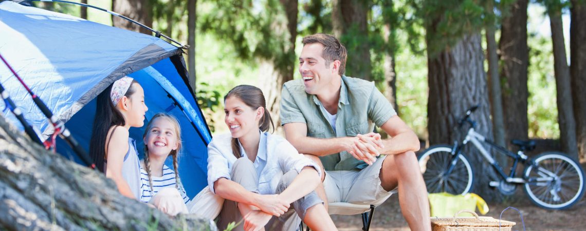 A family camping, sitting in front of a blue tent.