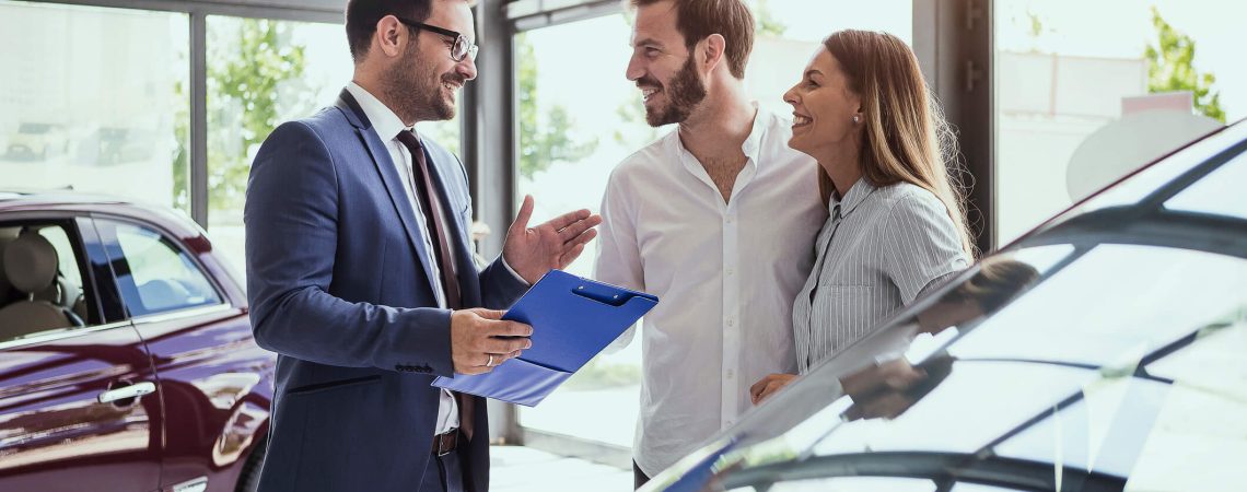 Business man talking to a couple at a car dealership