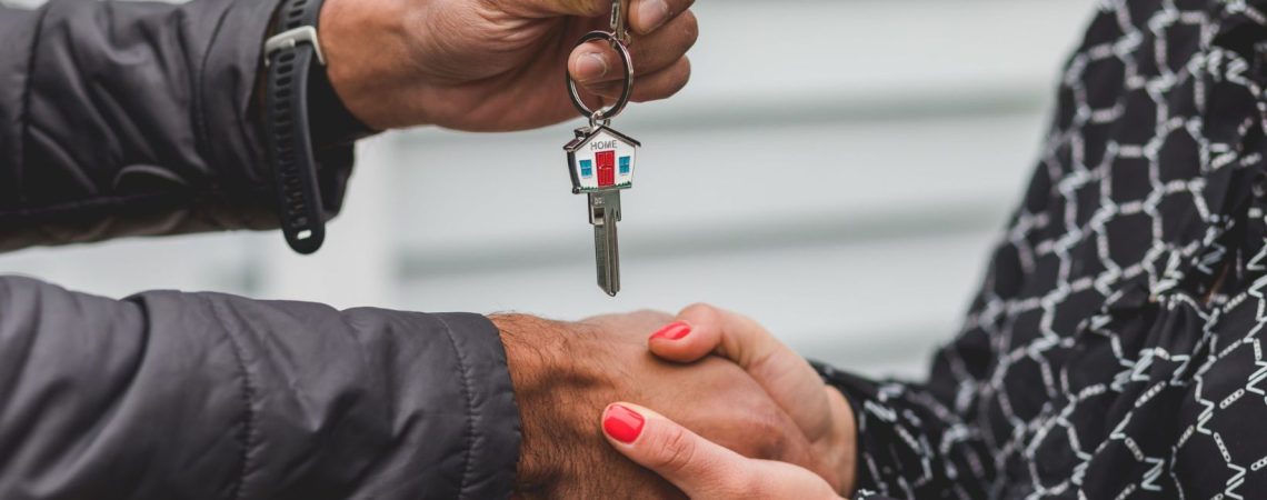 Two people shaking hands as the man hands a woman a house key.