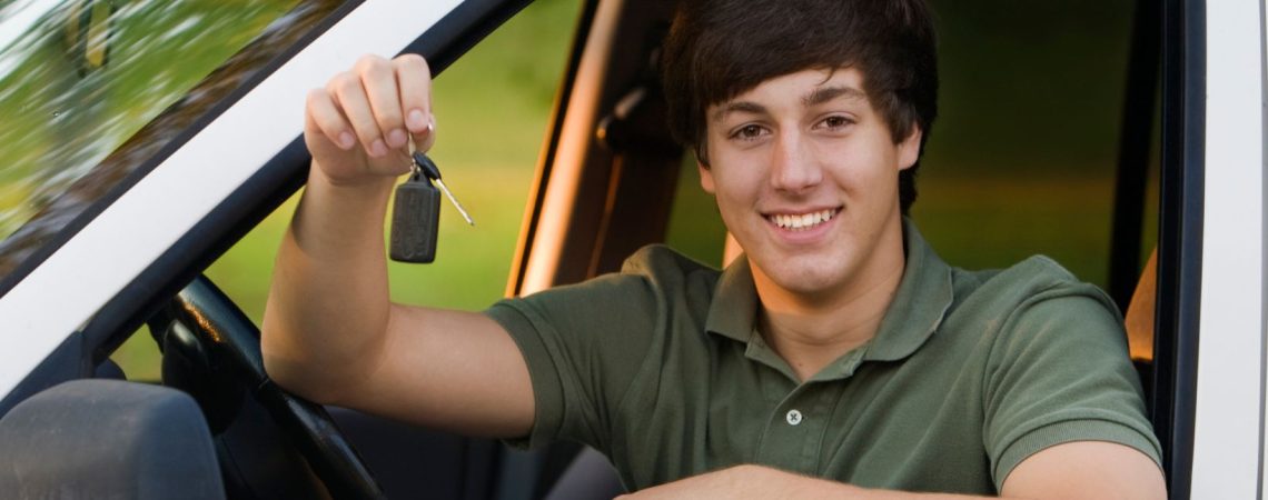 a teenager holding his car keys while sitting in the front seat of a car.