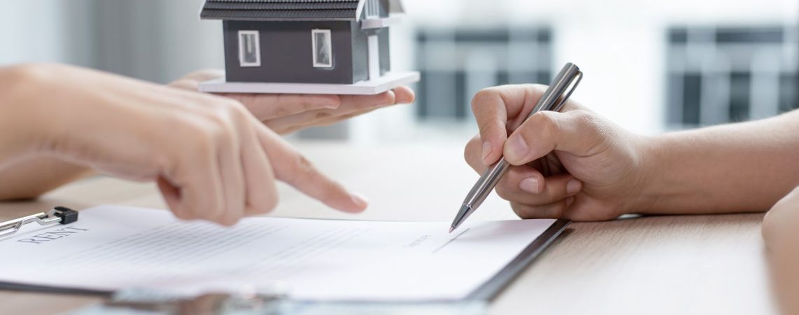 someone holding up a tiny home model while pointing to insurance papers.