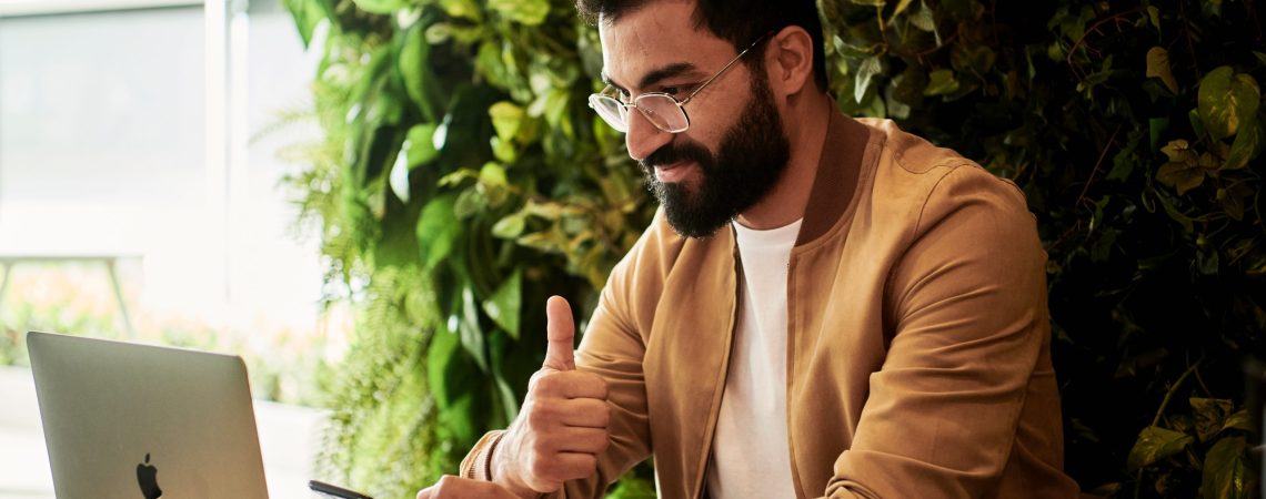 A man looking at a computer while giving thumbs up.