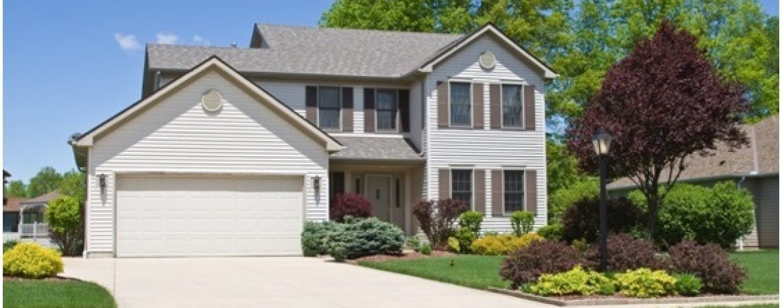 A white house surrounded by a beautiful lawn with a variety of bushes and trees.