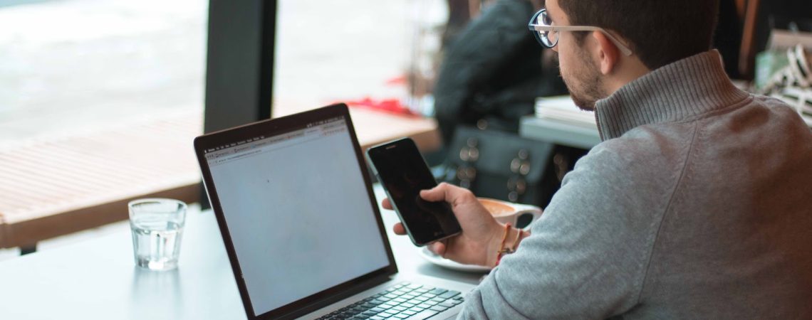 A man working on his laptop and holding his cell phone.