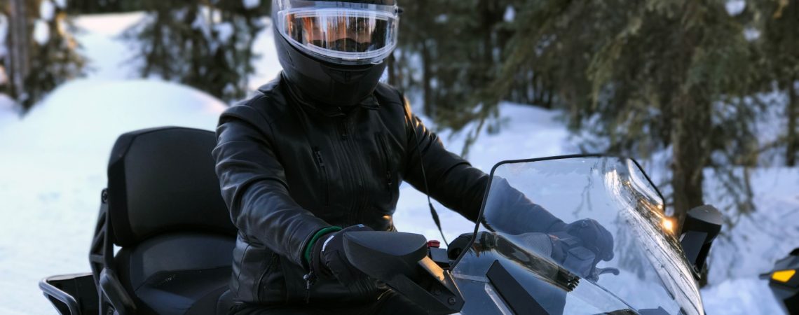 A person dressed in black with a black helmet riding a snowmobile.