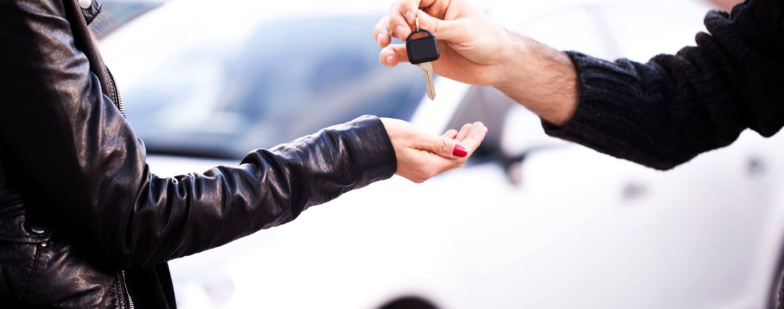 A person handing car keys to another person. With a white car in the background.