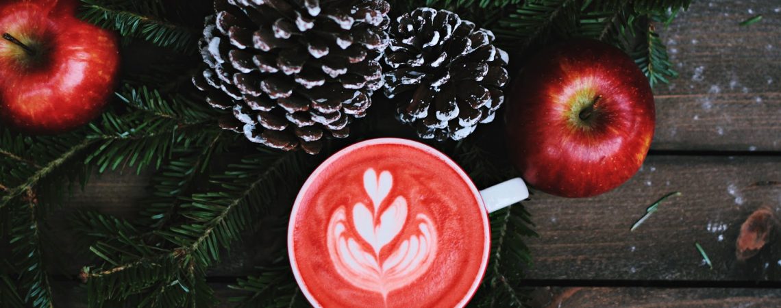 a holiday themed warm beverage surrounded by pine cones, cranberries and a garland