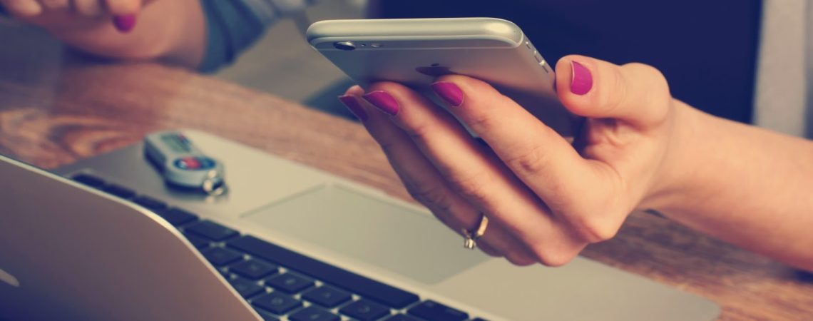 A woman holding her cell phone in front of a laptop.